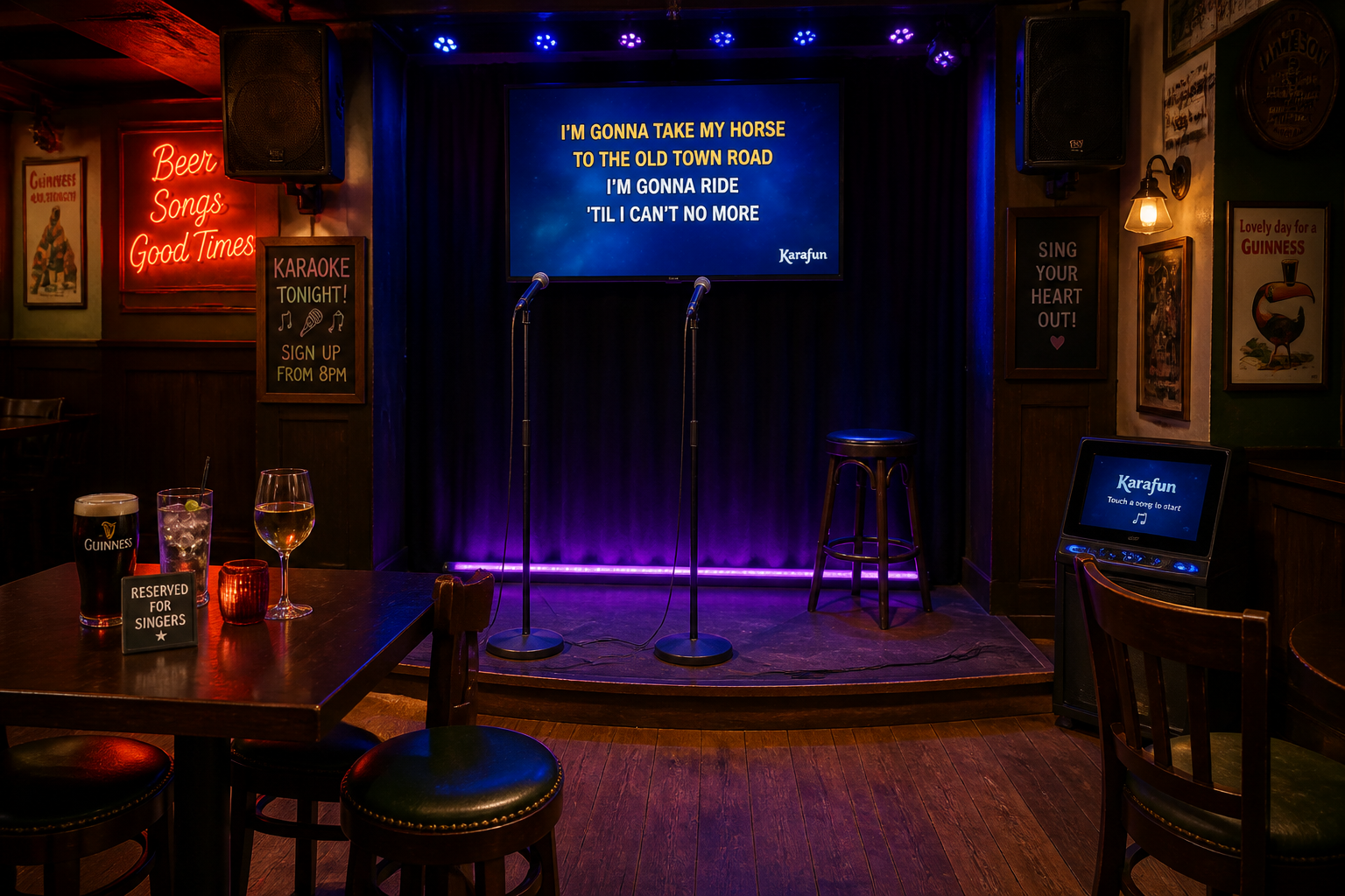 Small karaoke stage in a pub showing microphones, a drinks table and a lyric screen